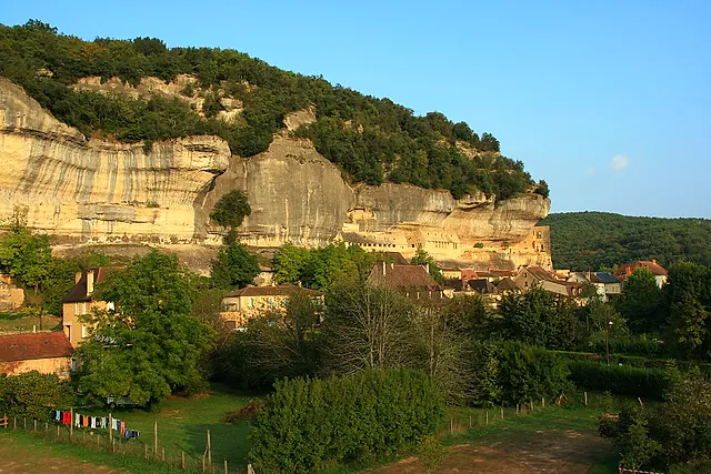 Die Kalksteinfelswand über dem Dorf Les Eyzies im Vézère-Tal, mit Häusern an ihrem Fuß im warmen Licht des späten Nachmittags