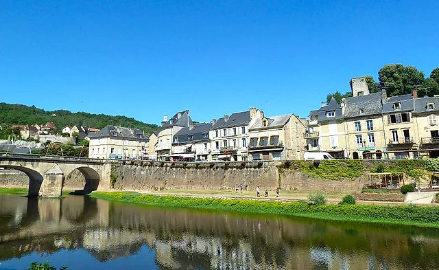 Die Steinbrücke über die Vézère in Montignac und die Häuser am Ufer, die sich unter blauem Himmel im ruhigen Wasser spiegeln