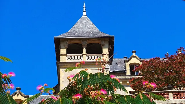 Ein schiefergedeckter Turm mit Loggia und Balustrade in Montignac, umrahmt von rosa Mimosenblüten vor tiefblauem Himmel