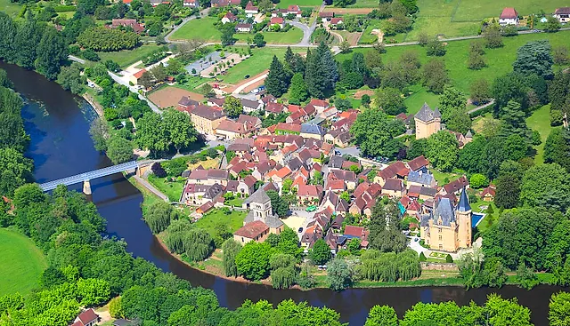 Luftaufnahme des Dorfes Saint-Léon-sur-Vézère in einer Flussschleife der Vézère, mit Brücke, Kirche und Schloss zwischen grünen Feldern