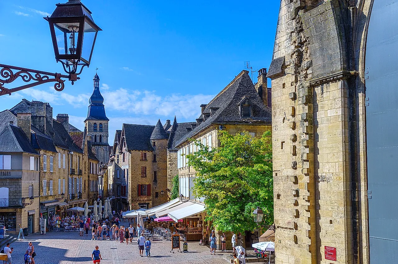 Place de la Liberté w Sarlat-la-Canéda, z miodowymi kamiennymi domami, dzwonnicą w oddali i kutą latarnią, pod błękitnym niebem