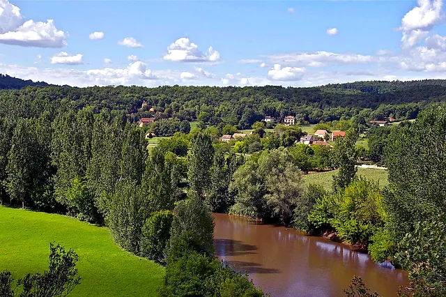 Die Vézère schlängelt sich durch grüne Wiesen und Wälder des Périgord, gesehen von La Roque Saint-Christophe, unter einem Himmel mit weißen Wolken
